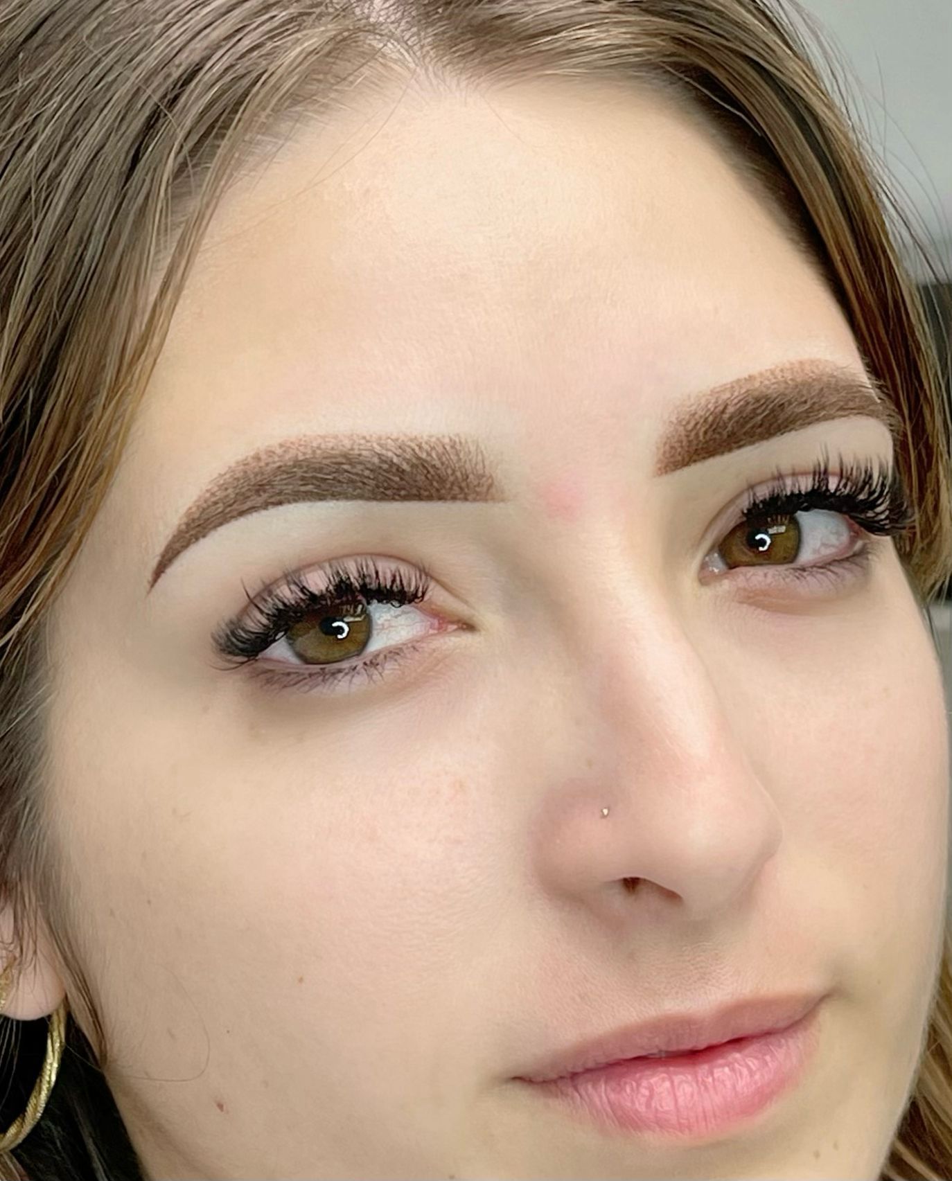 Woman with filled-in eyebrows, long eyelashes, and brown eyes. Facing forward with a slight smile.