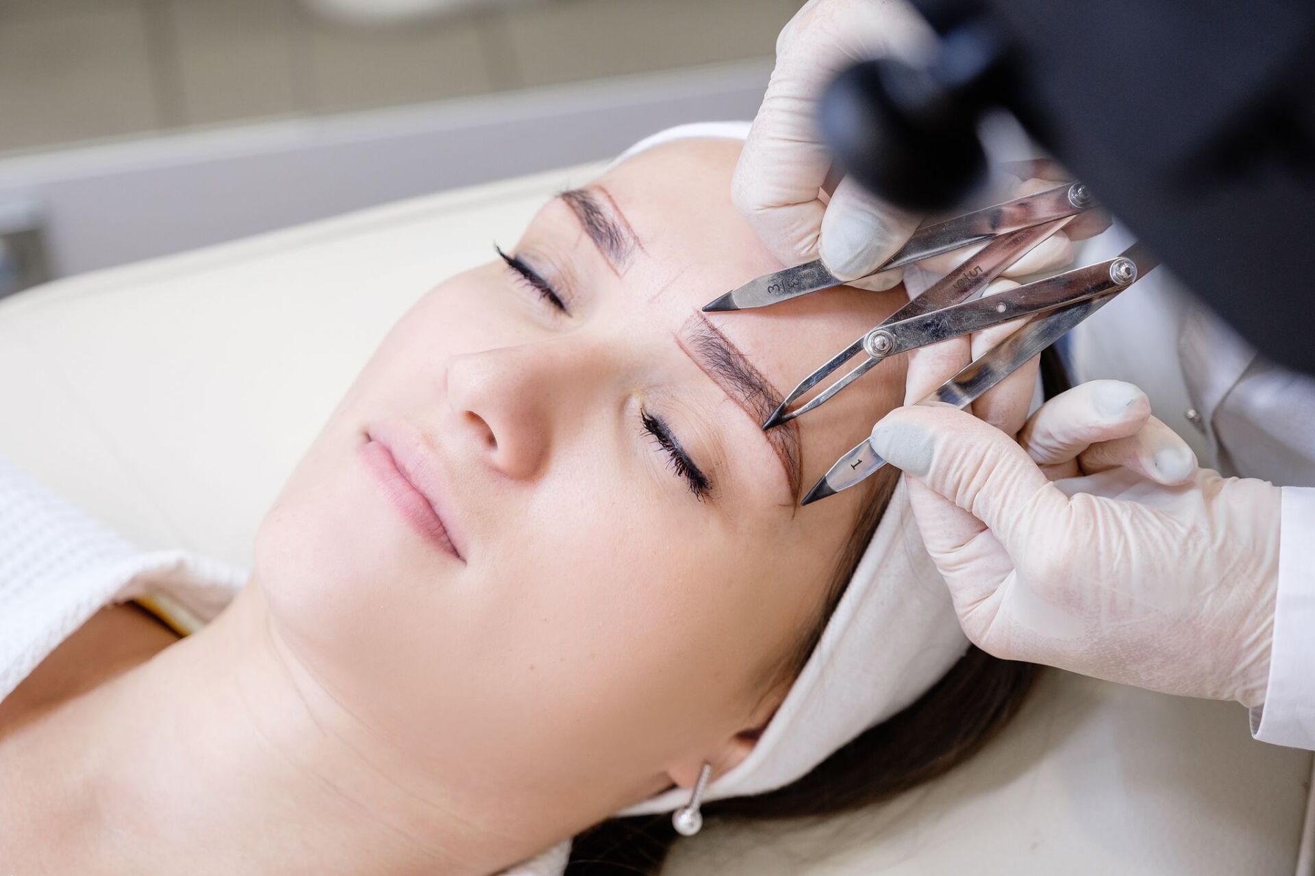 Woman getting eyebrow shaping with a tool in a beauty salon.