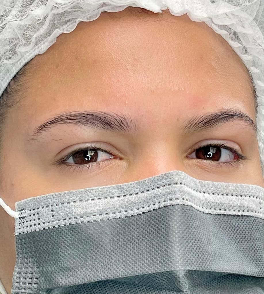 Woman wearing a surgical mask and hair net; eyes visible, eyebrows arched.