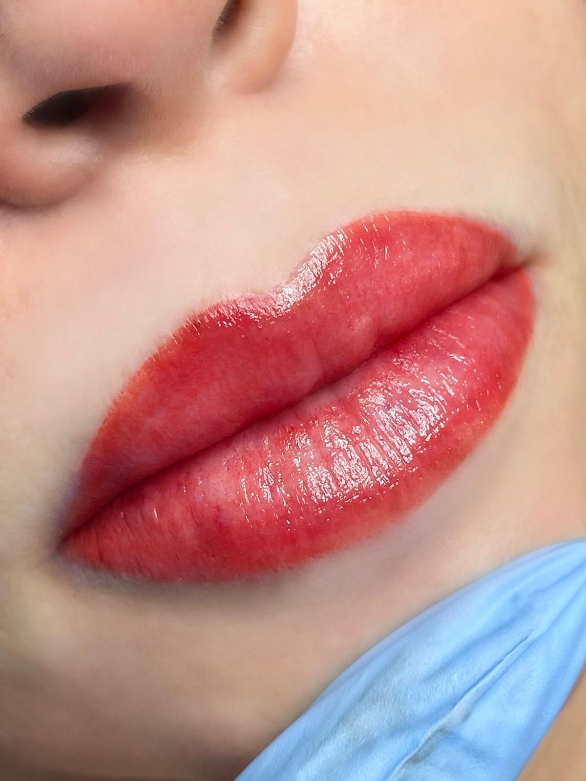 Close-up of full, glossy red lips with subtle shading, a gloved hand in the corner.