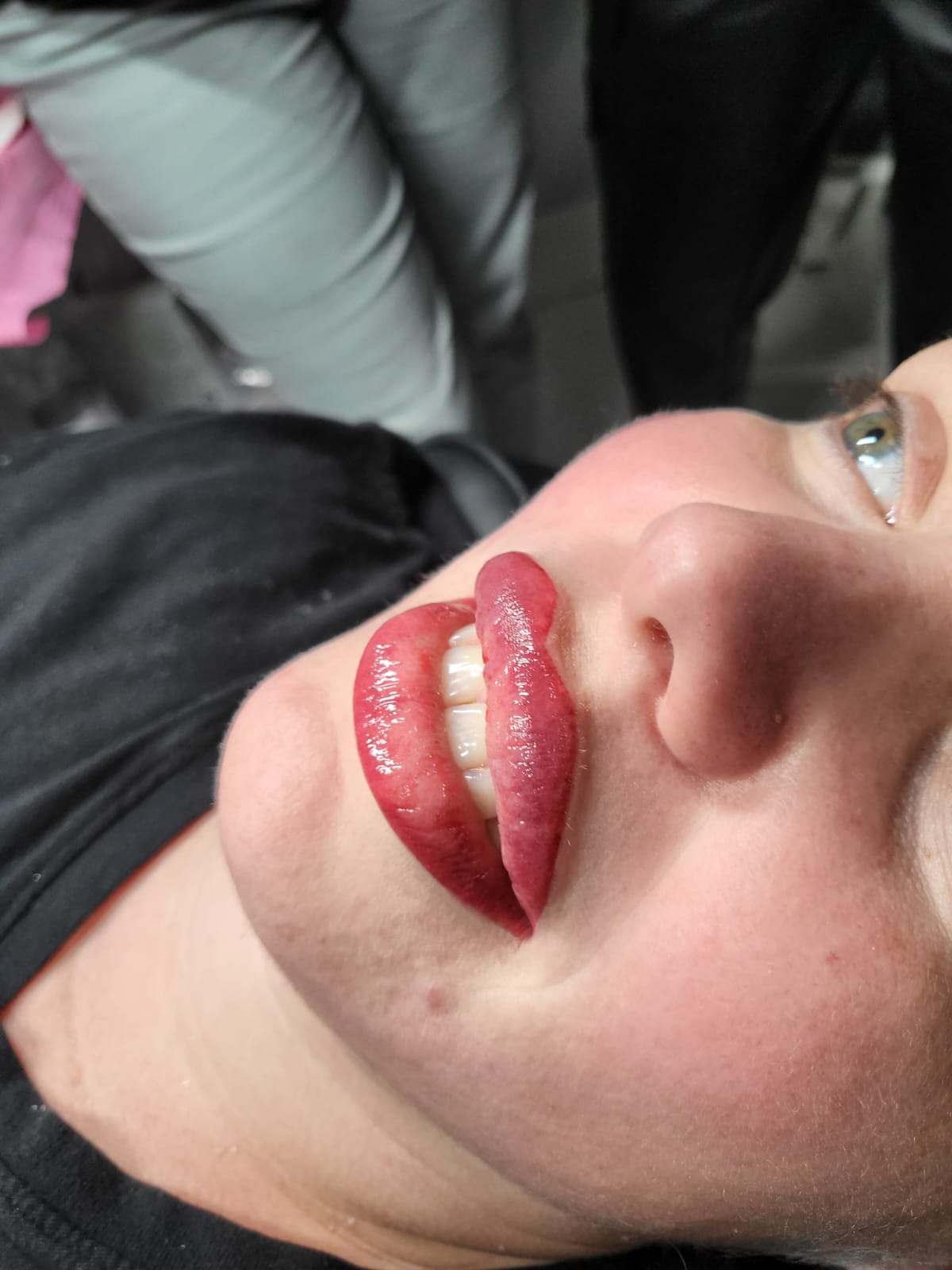 Woman with dark red lip tattoo, lying down. Lips are slightly open.