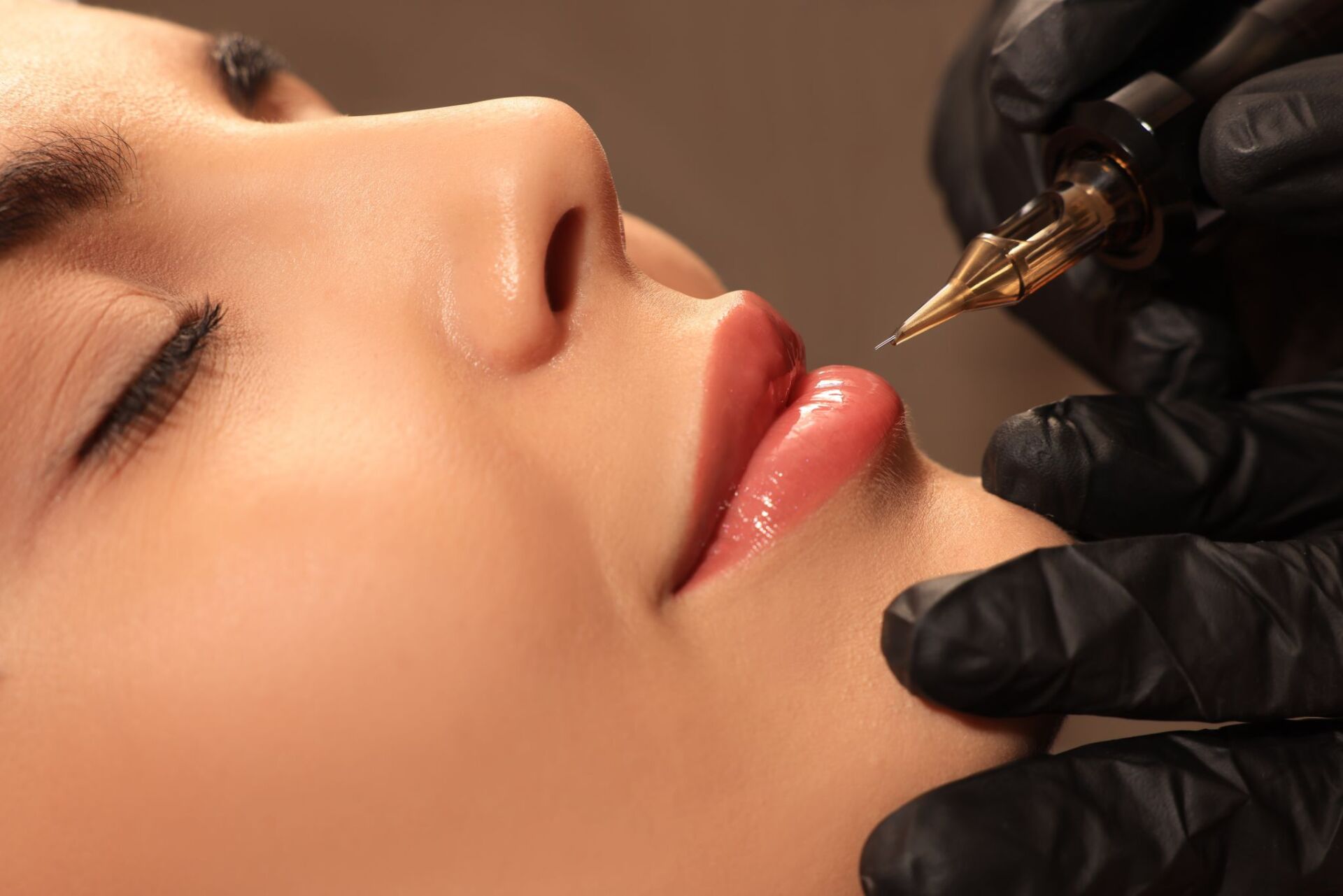 Lip blush tattoo procedure on woman's lips, close-up with needle and gloved hand.