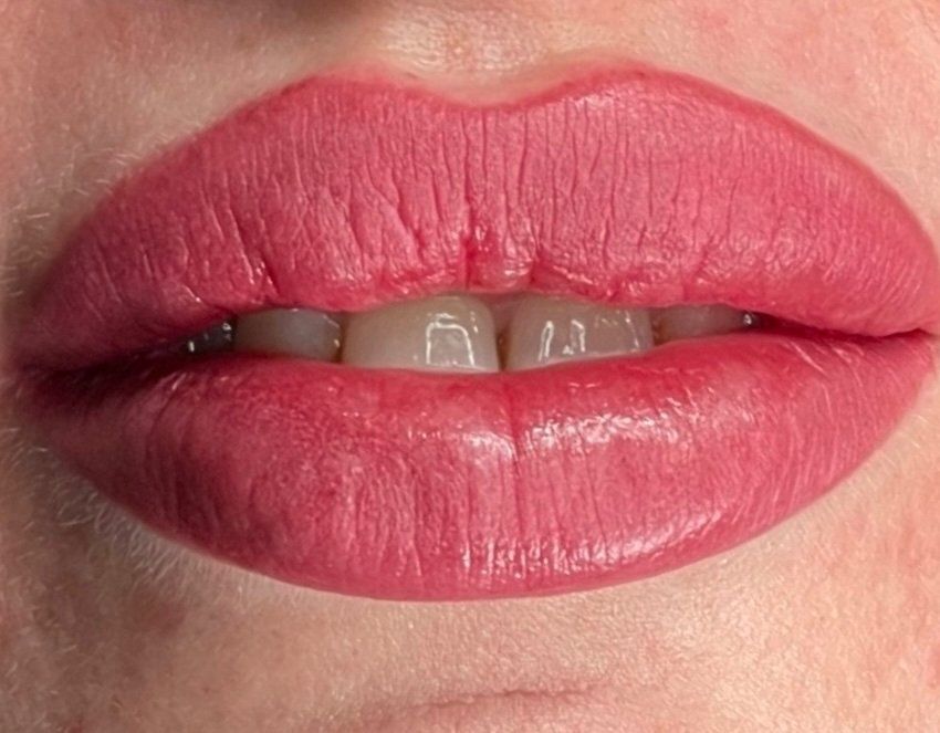 Close-up of pink lipstick on full lips, slightly parted, revealing white teeth.