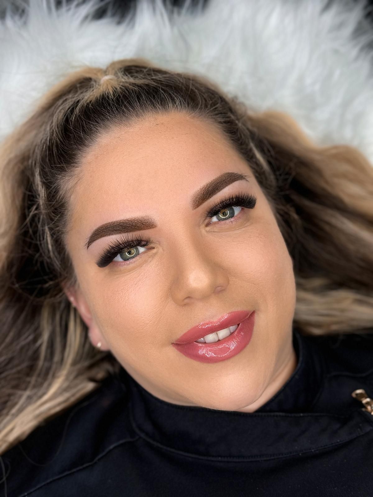Woman with brown, shaded eyebrows, long eyelashes, and glossy lips.