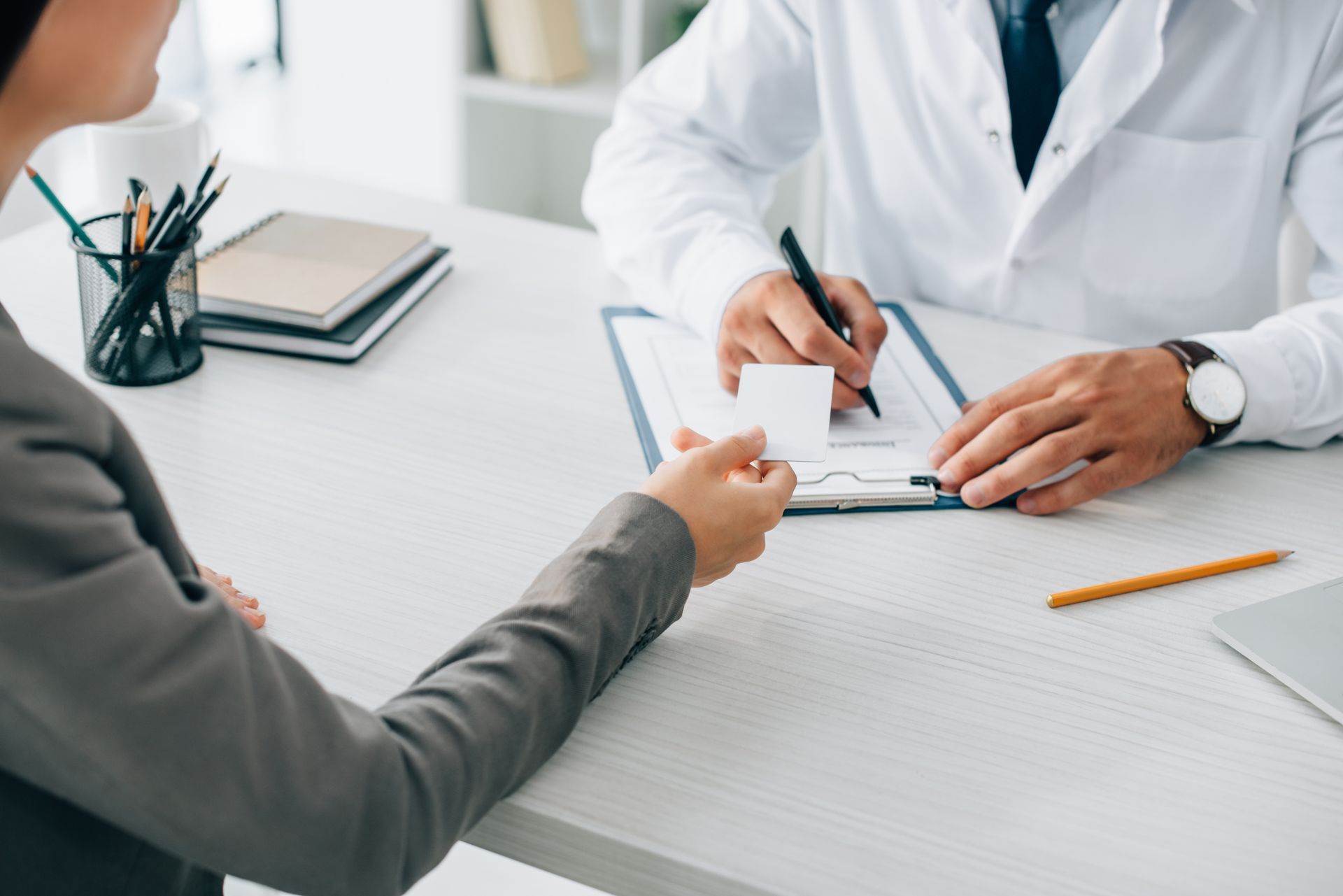 A worker is explaining the form to a man. Doctor writing prescription and handing card to patient during medical office consultation.