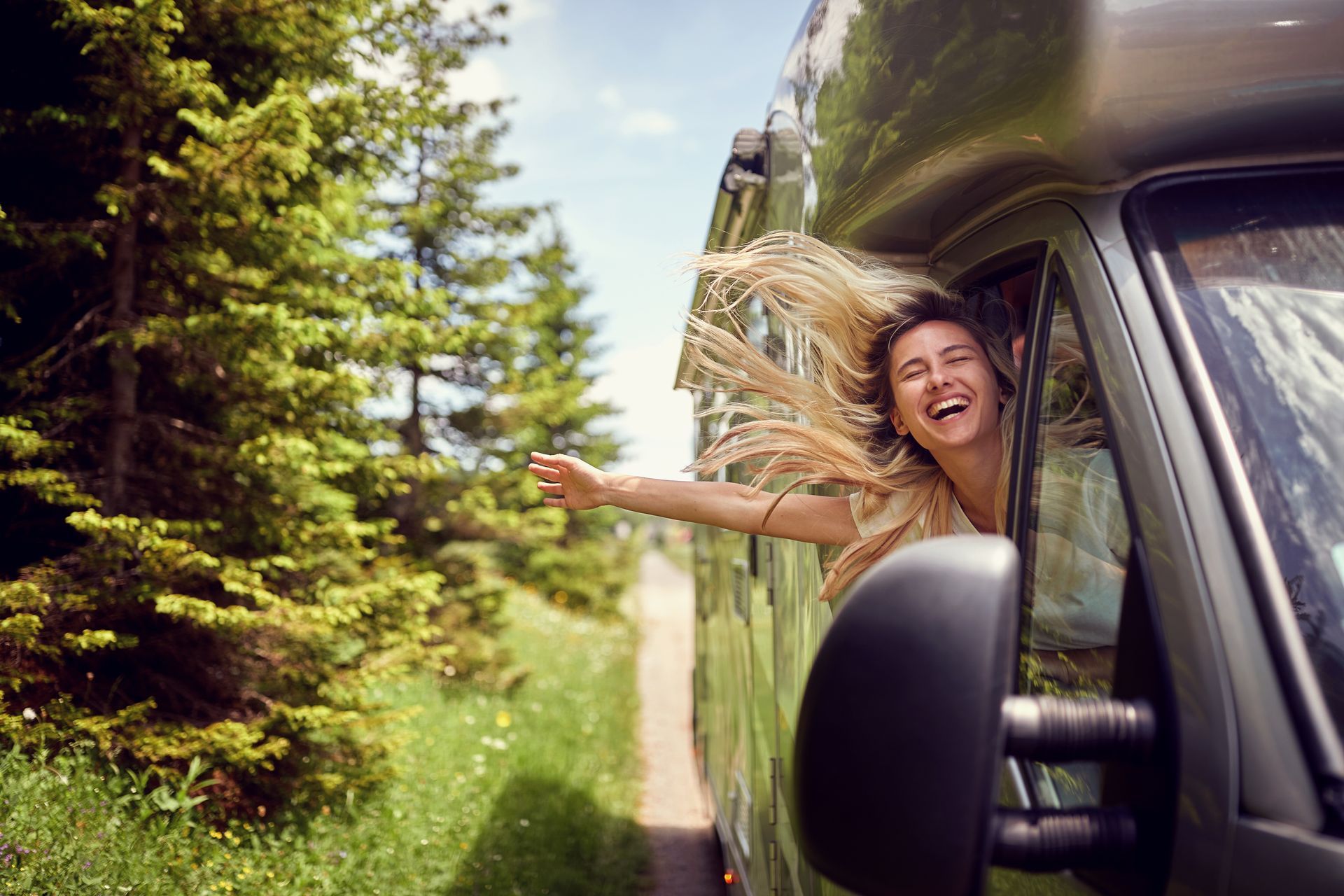 Woman handing receptionist medical insurance card at MRI clinic reception Smiling woman leaning out of a moving RV window on a forest road, enjoying her RV insurance package.