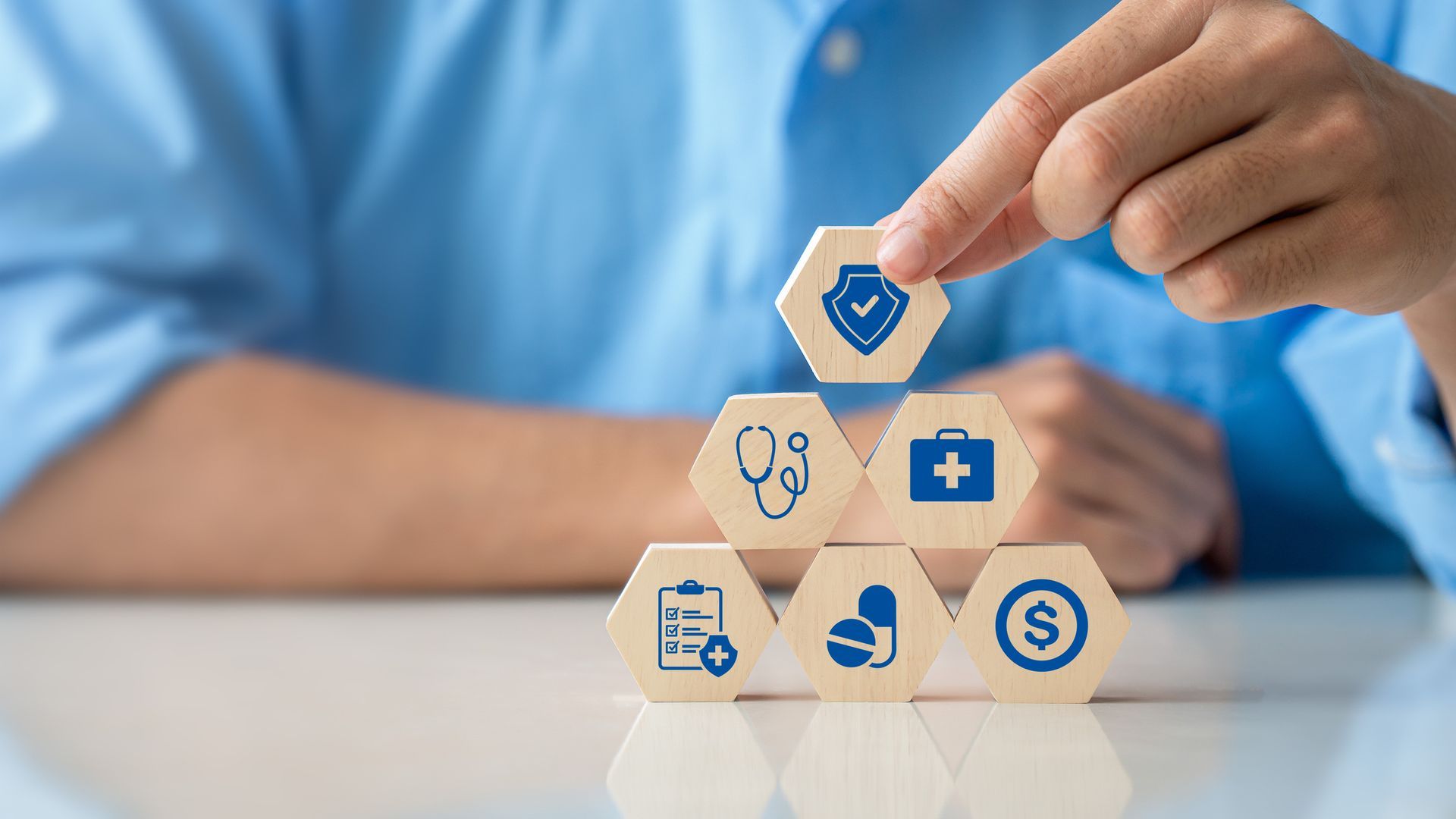 Hand stacking wooden blocks with healthcare icons.