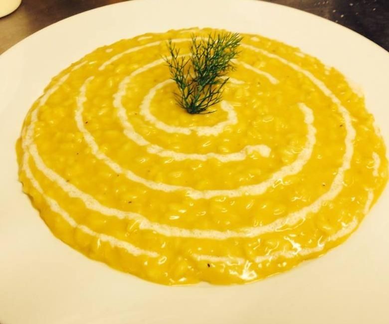 Un piatto bianco condito con una salsa gialla e un rametto di aneto