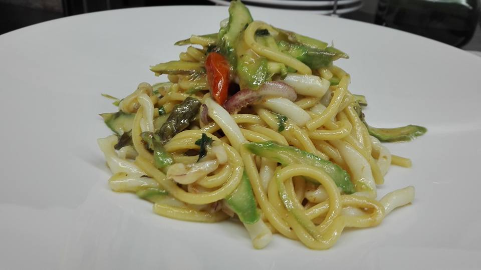 Un piatto bianco con sopra tagliatelle e verdure su un tavolo.