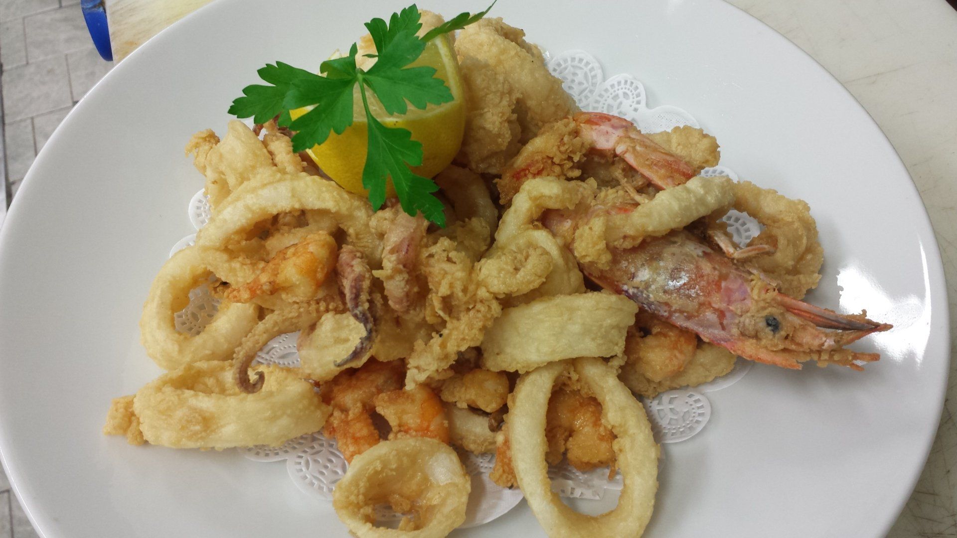 Un piatto bianco guarnito con frutti di mare fritti e uno spicchio di limone.