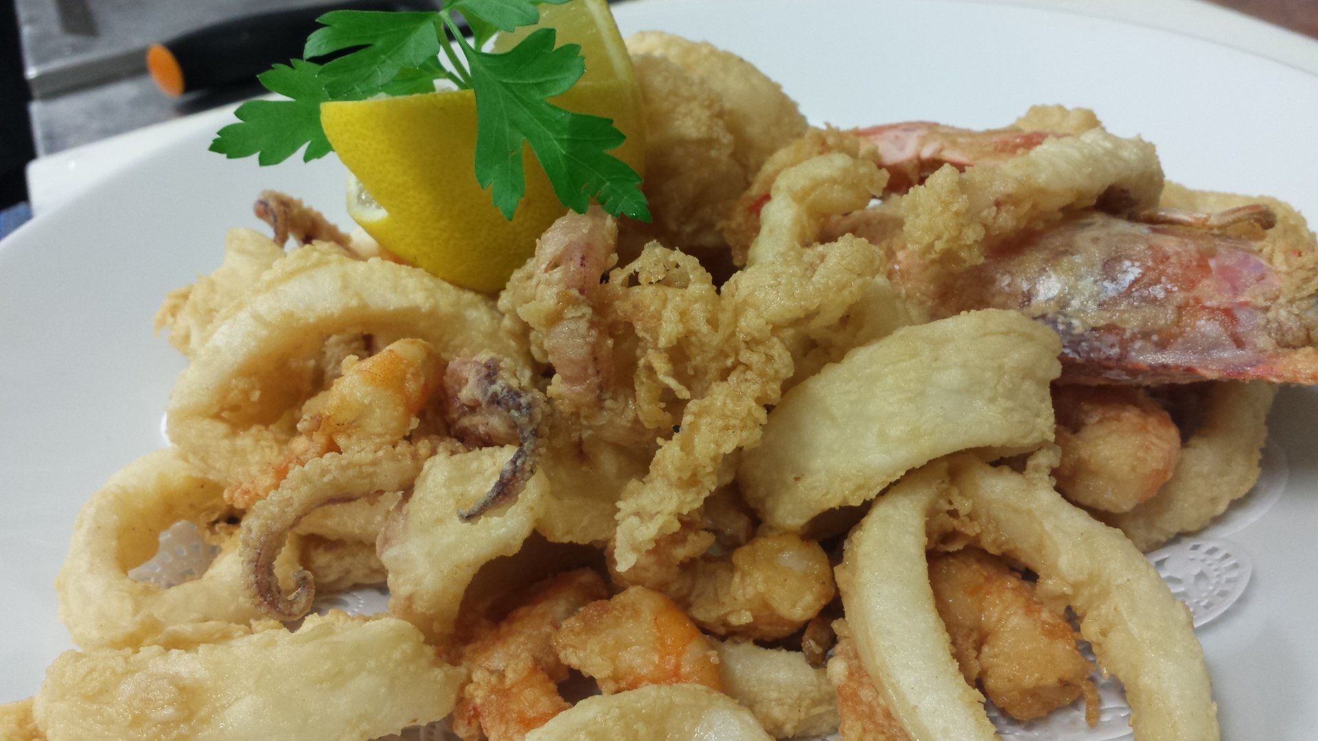Un piatto bianco guarnito con frutti di mare fritti e uno spicchio di limone.