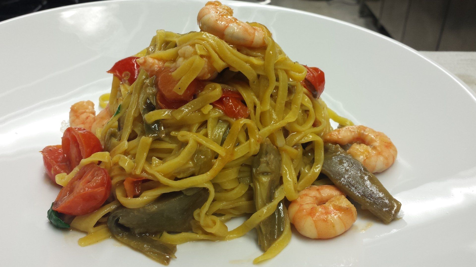 Un piatto bianco con sopra tagliatelle, gamberi e pomodori