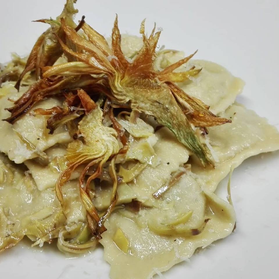 Un piatto bianco con ravioli e carciofi su un tavolo.