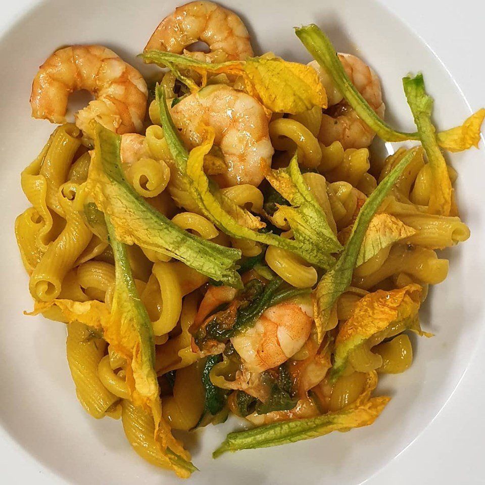 Un piatto bianco condito con pasta, gamberi e verdure