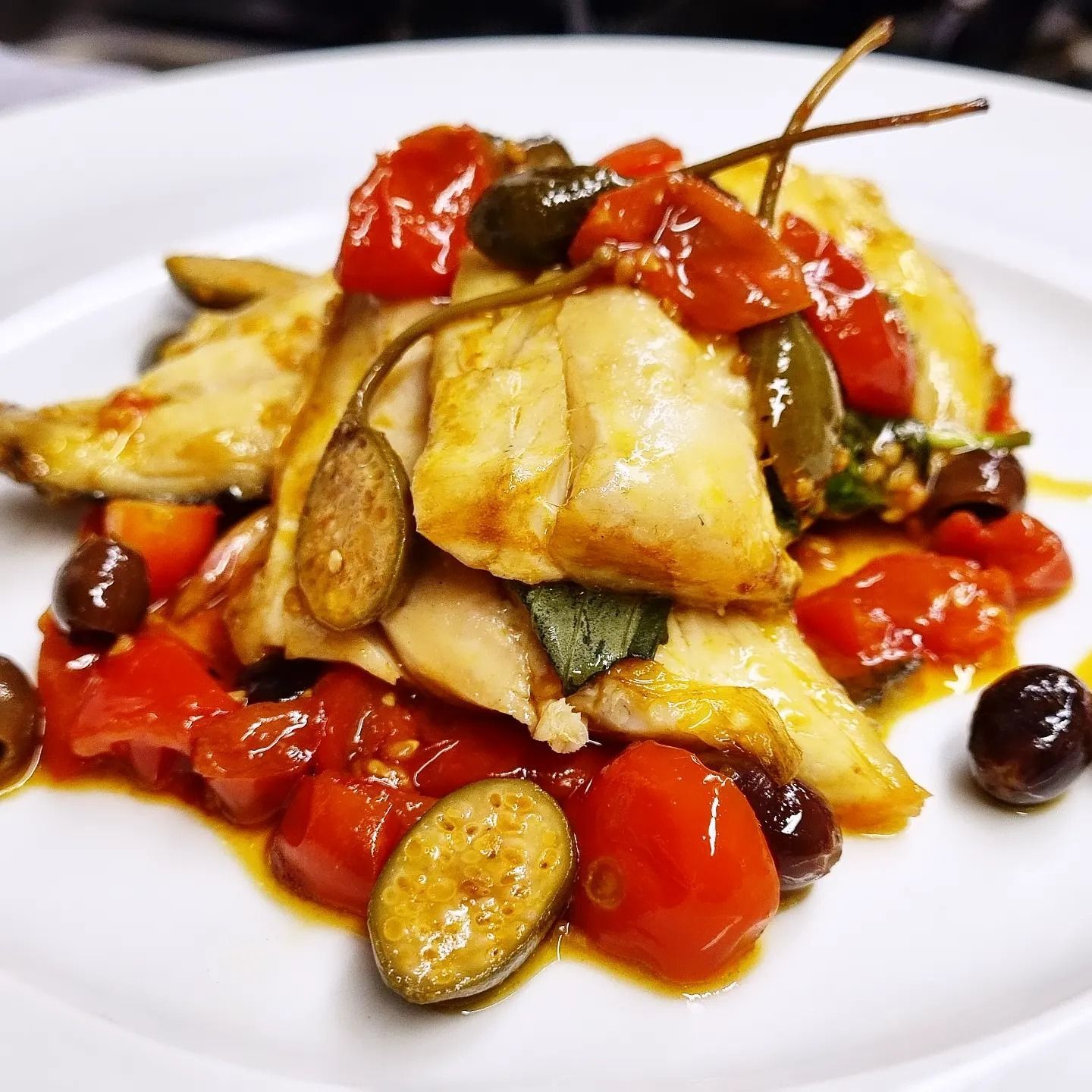 Un piatto bianco condito con pollo, olive e pomodori