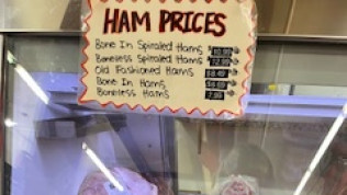 A sign that says ham prices hangs above a meat case.
