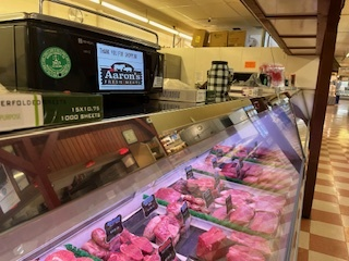 A butcher 's display case filled with meat and a sign that says aaron 's