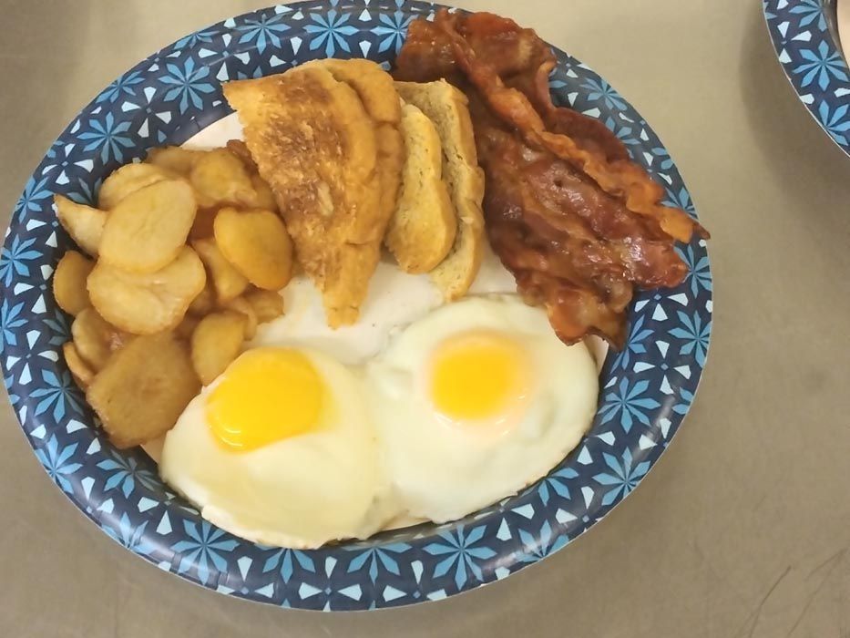 A paper plate with eggs bacon and potatoes on it