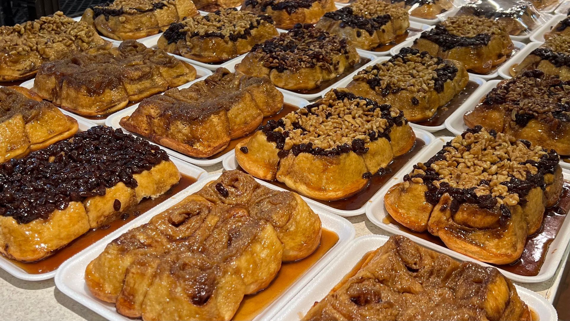 A bunch of cinnamon rolls on styrofoam trays on a table.
