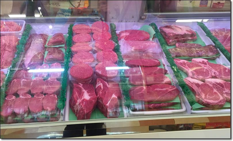 A variety of meats are displayed in a glass case.
