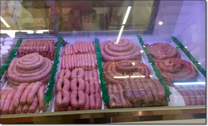 A variety of sausages are displayed in a glass case.