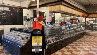A woman is standing in front of a display case in a grocery store.