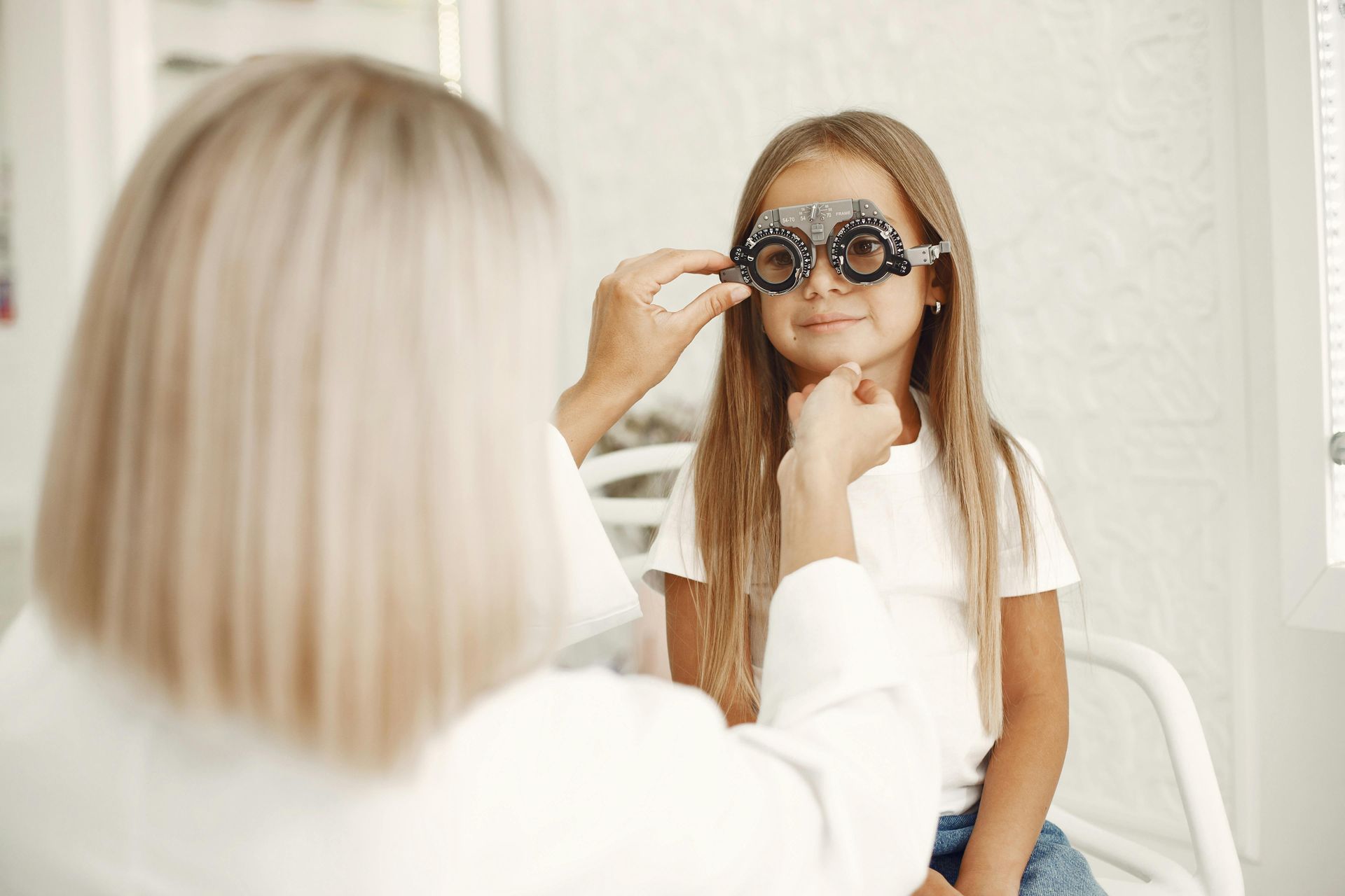 Hands trying on black eyeglasses in a display of assorted frames on a wall