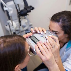 Eye exam with a patient looking into a diagnostic machine as an optometrist adjusts it