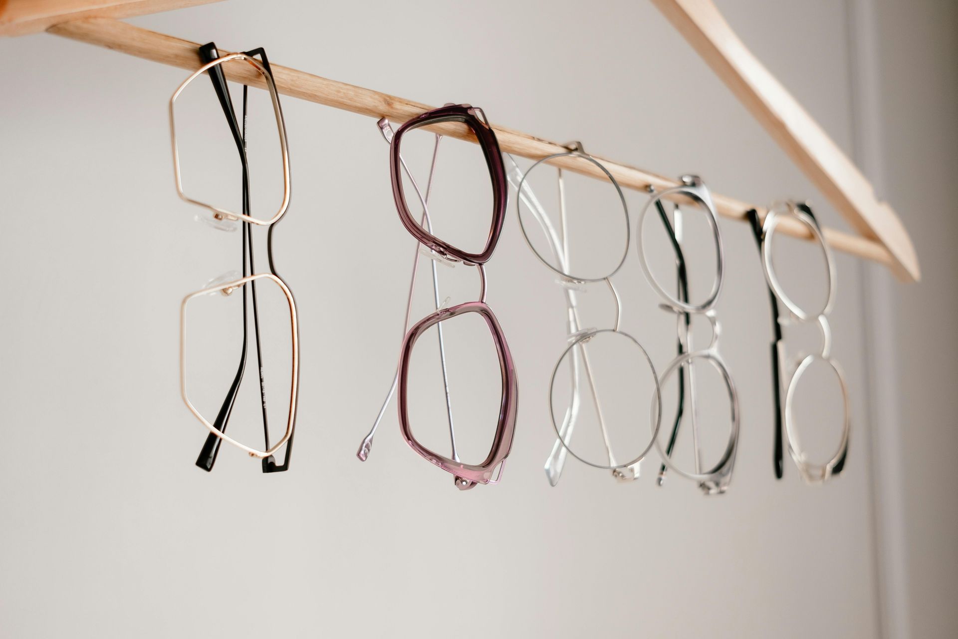 Hands trying on black eyeglasses in a display of assorted frames on a wall