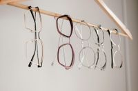 Hands trying on black eyeglasses in a display of assorted frames on a wall