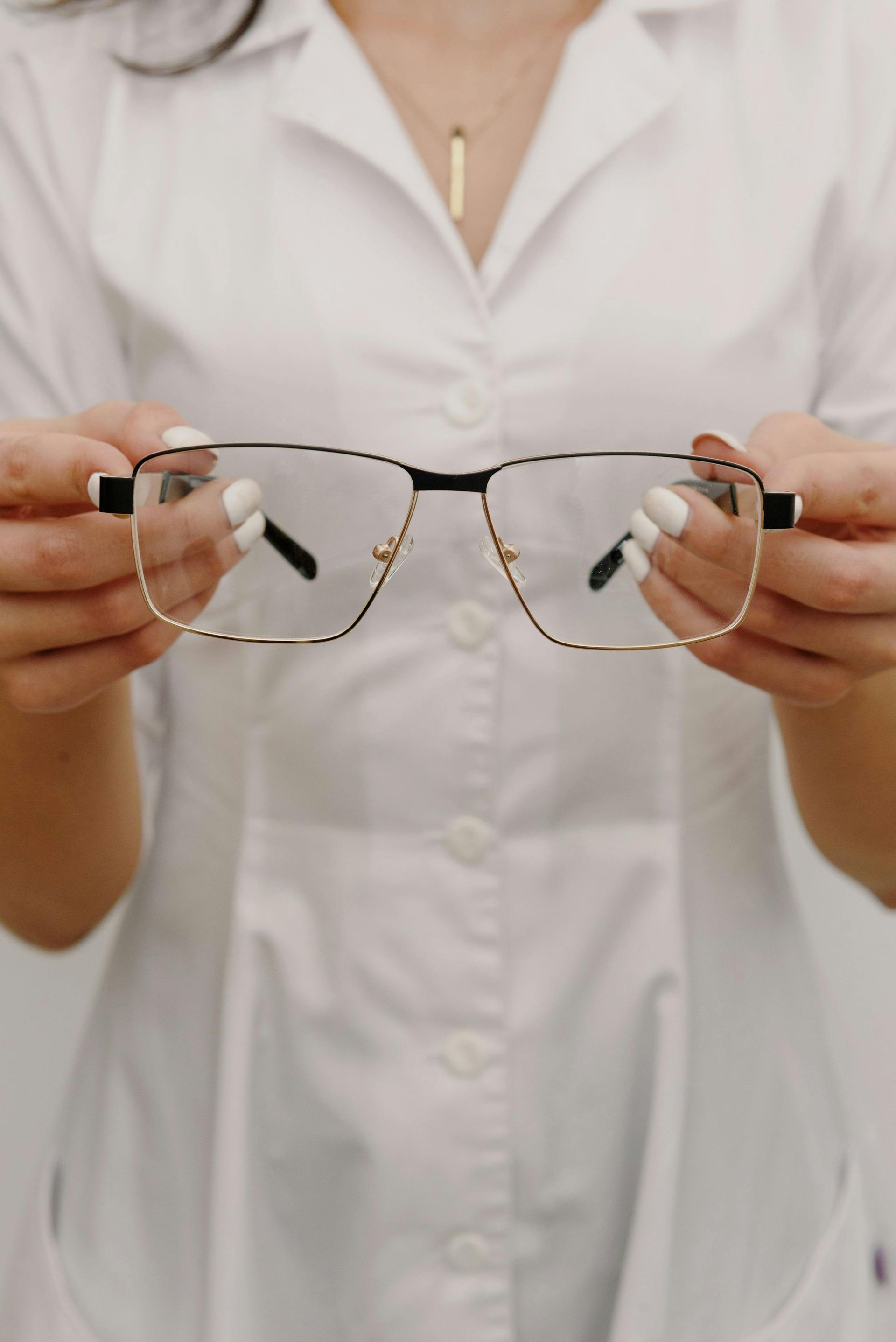 Hands trying on black eyeglasses in a display of assorted frames on a wall