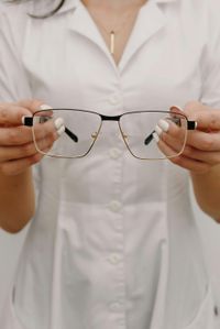 Hands trying on black eyeglasses in a display of assorted frames on a wall