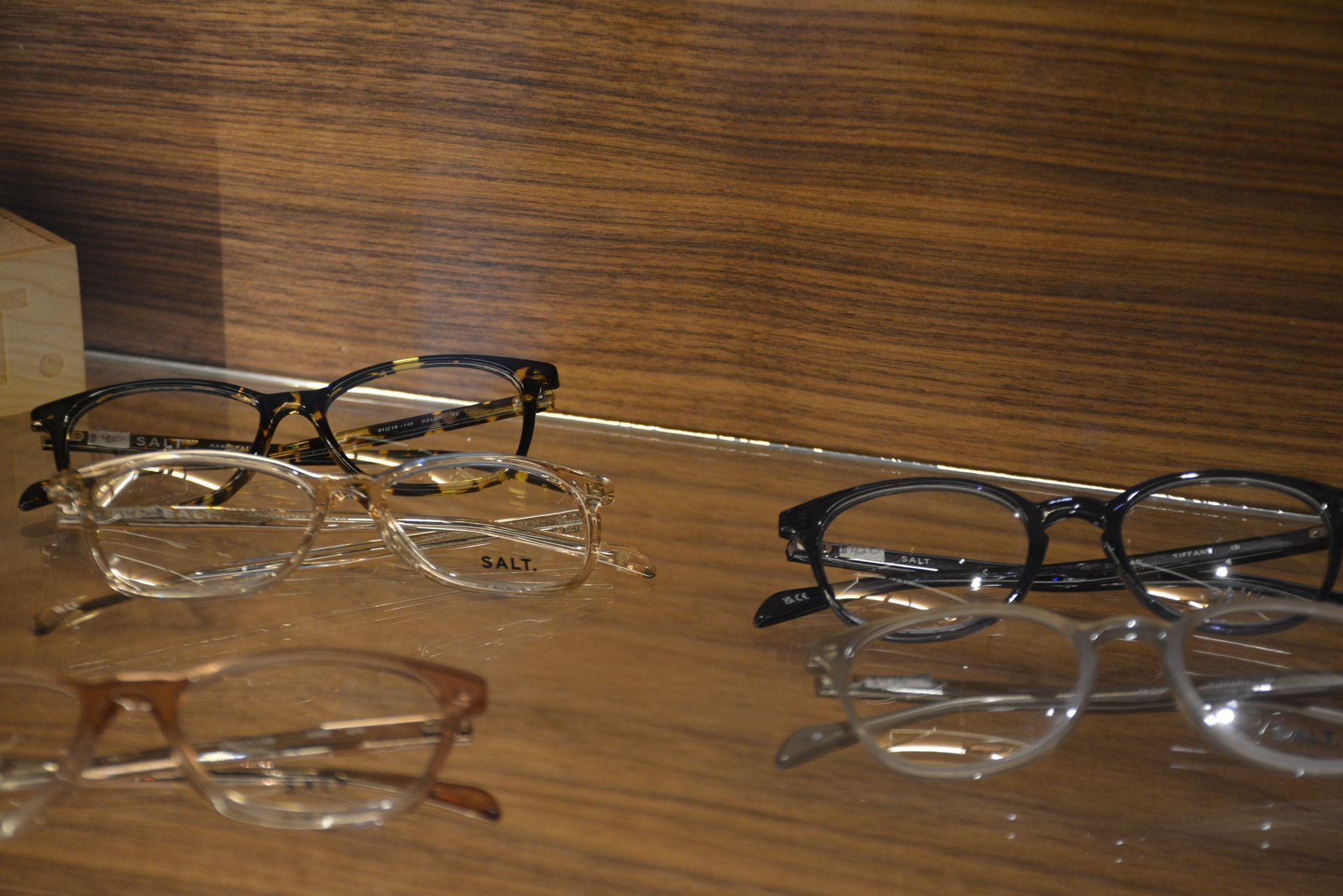 Hands trying on black eyeglasses in a display of assorted frames on a wall