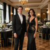 Una pareja elegantemente vestida posando en un elegante salón de baile con candelabros y mesas de banquete.