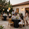 Cena al aire libre en un patio con guirnaldas de luces, globos e invitados sentados alrededor de mesas negras.
