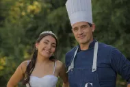 Dos personas con delantales y gorros de chef sonriendo al aire libre en un entorno ajardinado.