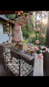 Pastel de bodas floral rosa sobre una mesa de postres decorada con cristalería y flores al aire libre.