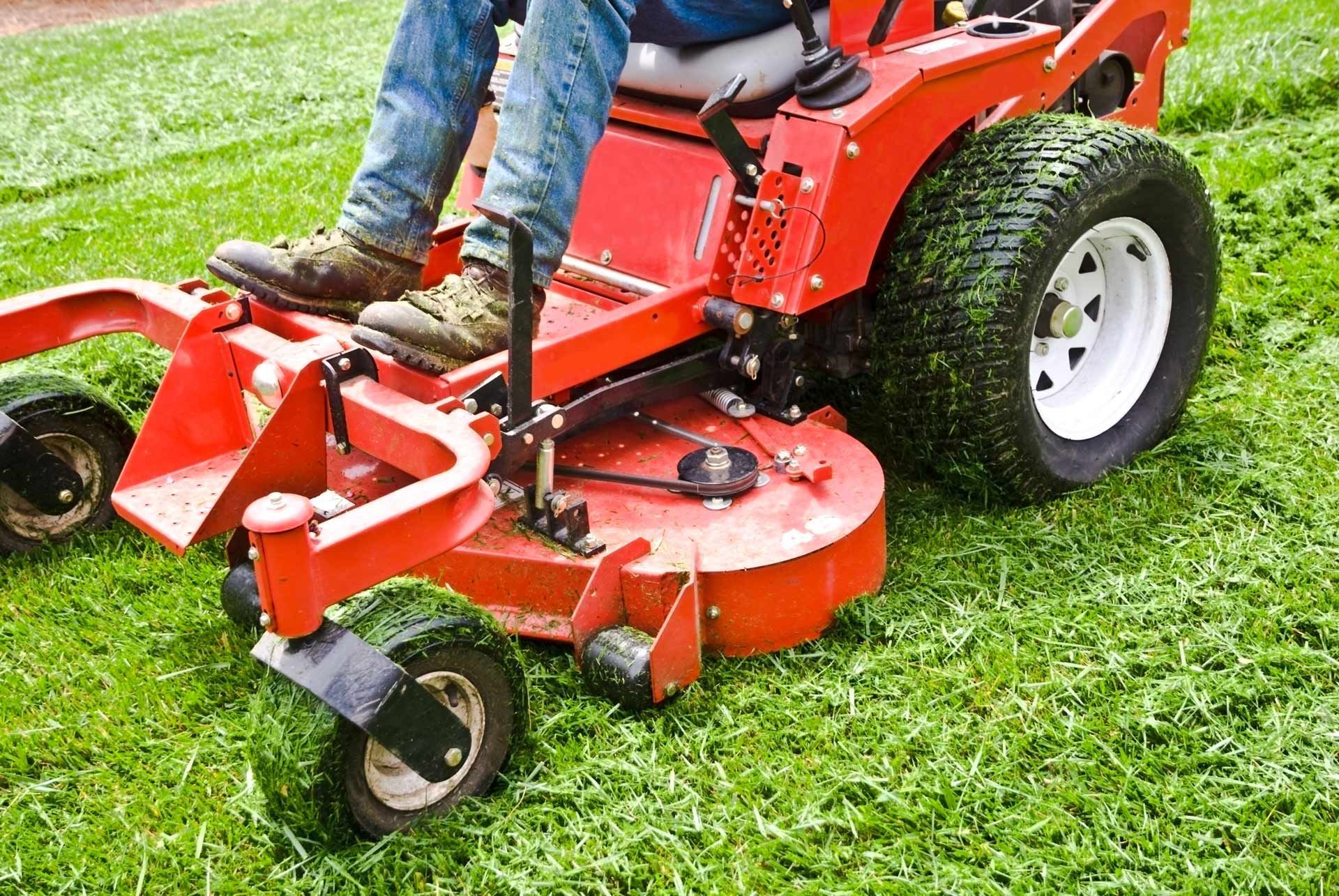 Person operating a red zero-turn lawn mower on a grassy lawn.