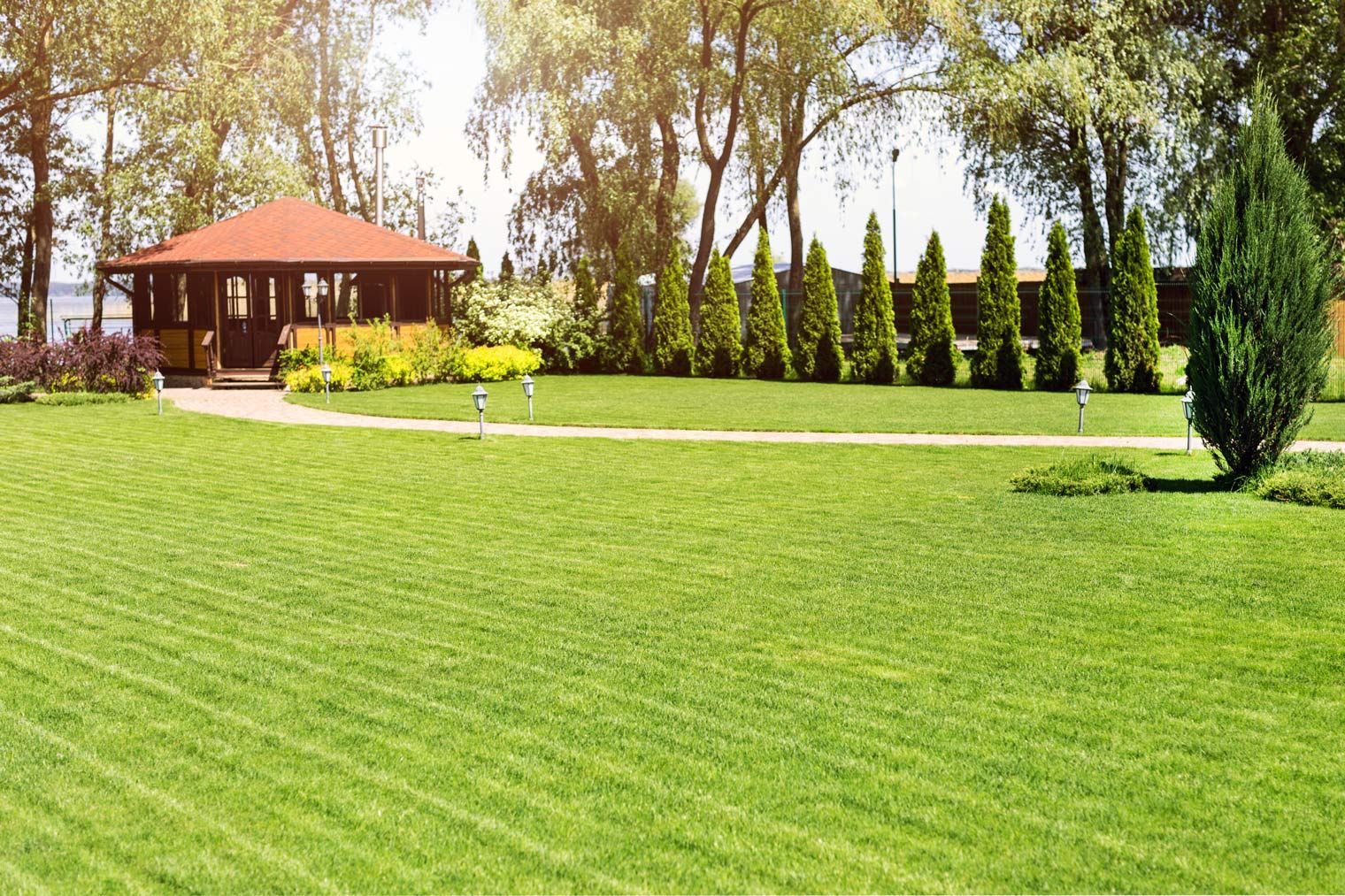 Lush green lawn with a gazebo and trees in a sunny outdoor setting.