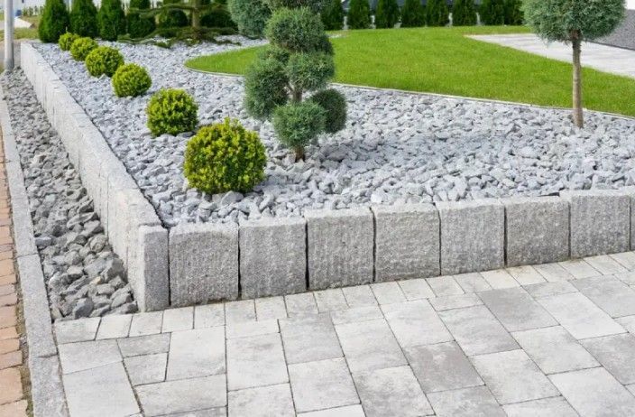 Stone-edged garden bed with gray gravel, various green shrubs, and paved pathway. Stone-edged garden bed with gray gravel, various green shrubs, and paved pathway.