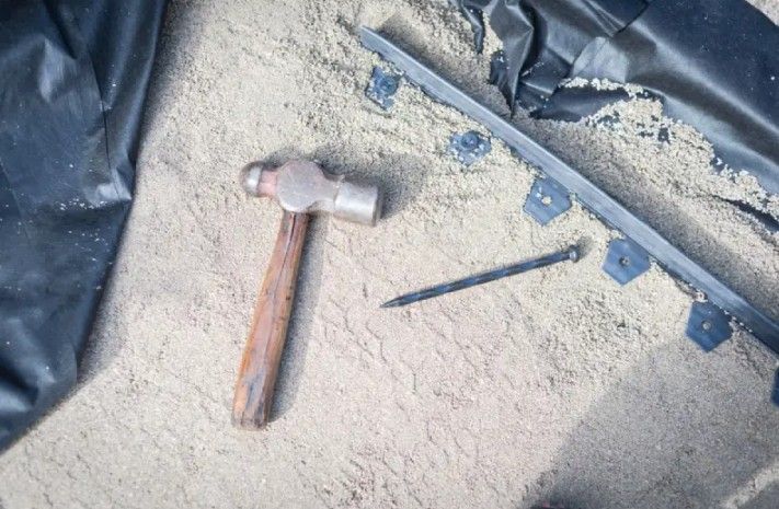 Hammer and nail on sand, next to black landscape edging and a plastic sheet. Hammer and nail on sand, next to black landscape edging and a plastic sheet.