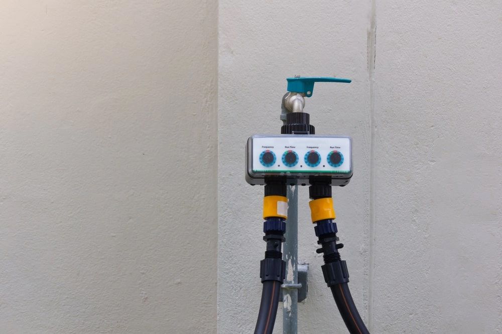 Water faucet with a 4-zone timer controller and hoses attached against a light-colored wall. Water faucet with a 4-zone timer controller and hoses attached against a light-colored wall.