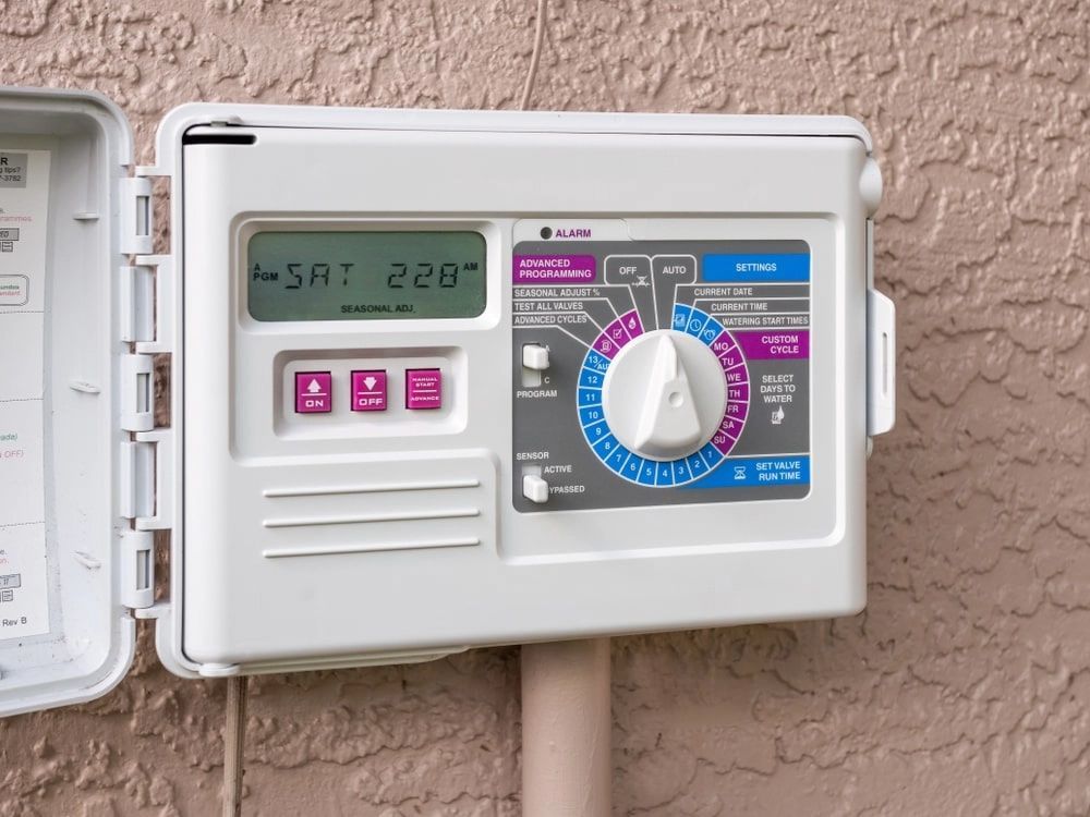 White sprinkler system control panel on a light brown stucco wall, dial set to water. White sprinkler system control panel on a light brown stucco wall, dial set to water.