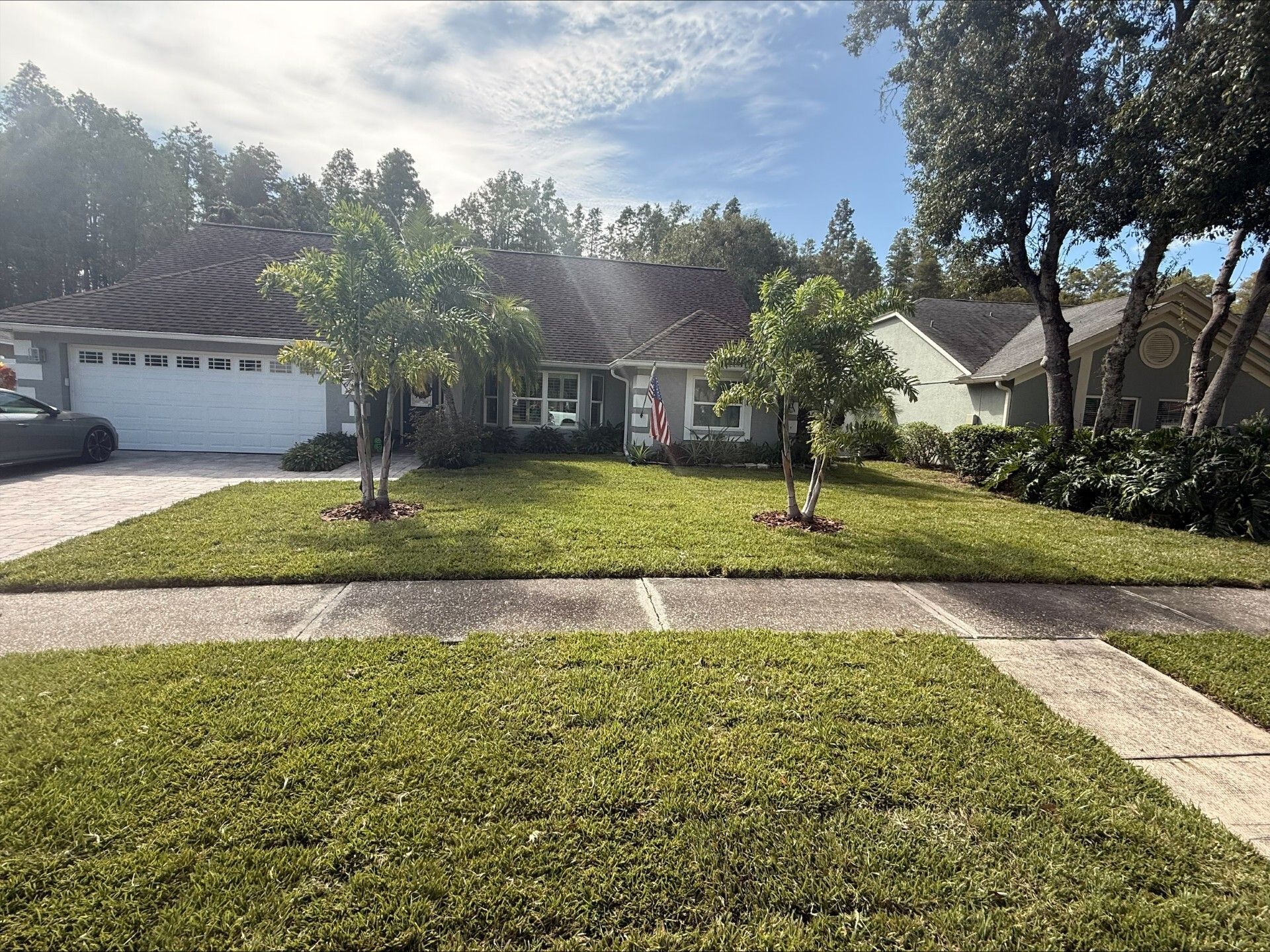 House with green lawn, trees, and driveway under a sunny sky.