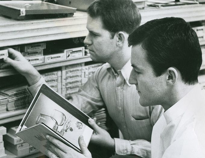 Two men are looking at a book together in a black and white photo