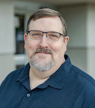 A man wearing glasses and a plaid shirt is smiling for the camera.
