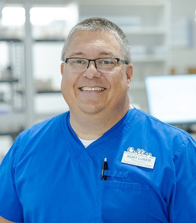 A man with a beard is wearing a white lab coat and blue scrubs.