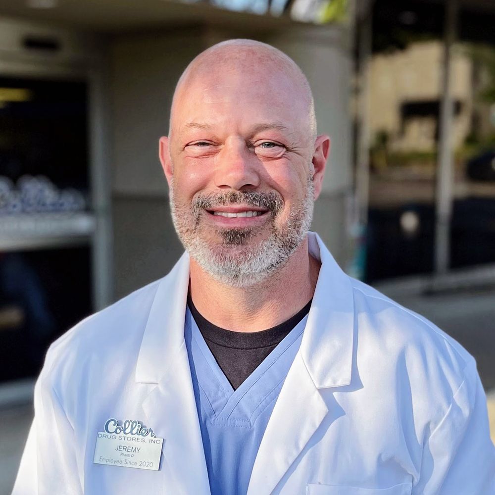 A bald man with a beard is wearing a white lab coat and smiling.