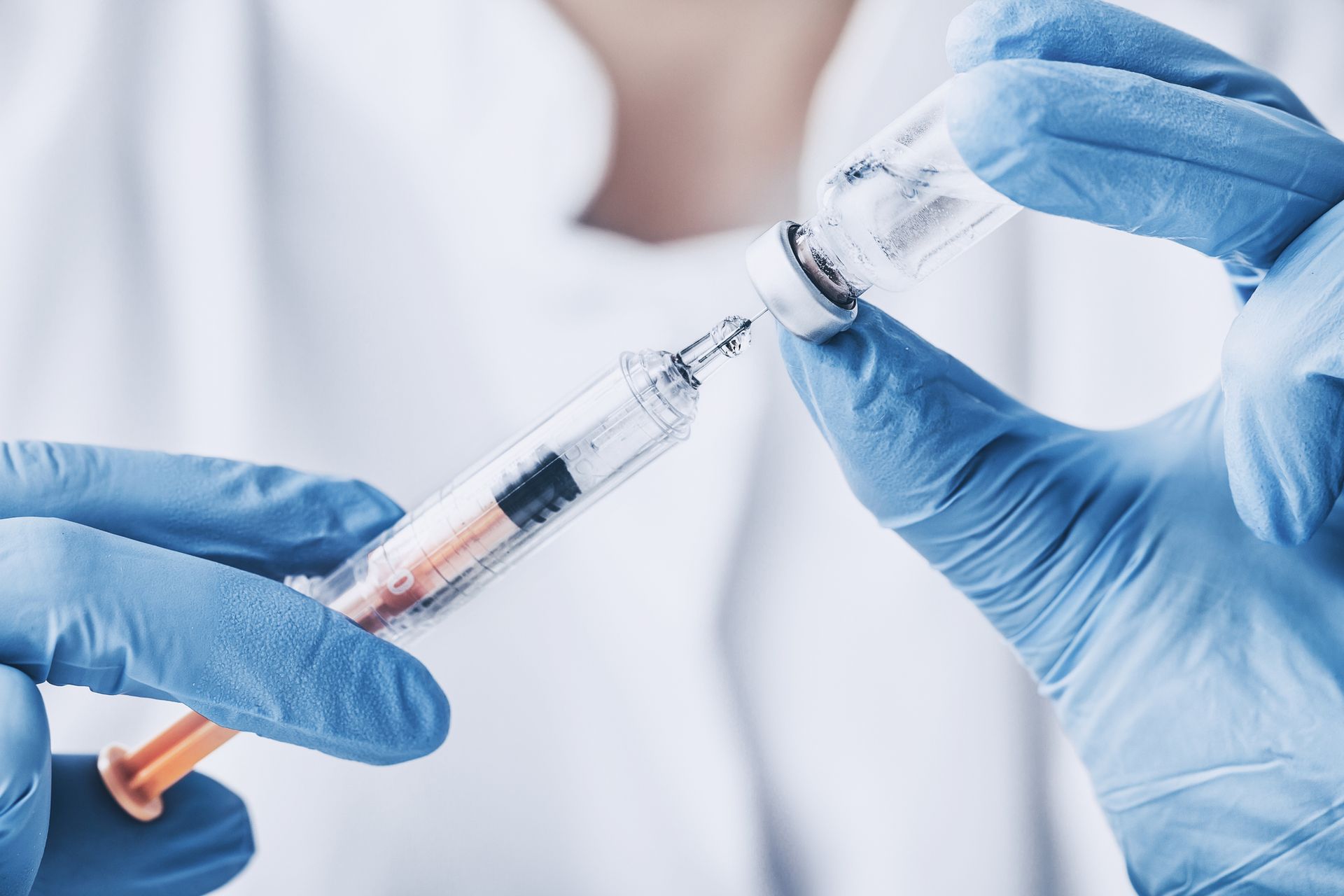 A person wearing blue gloves is holding a syringe.
