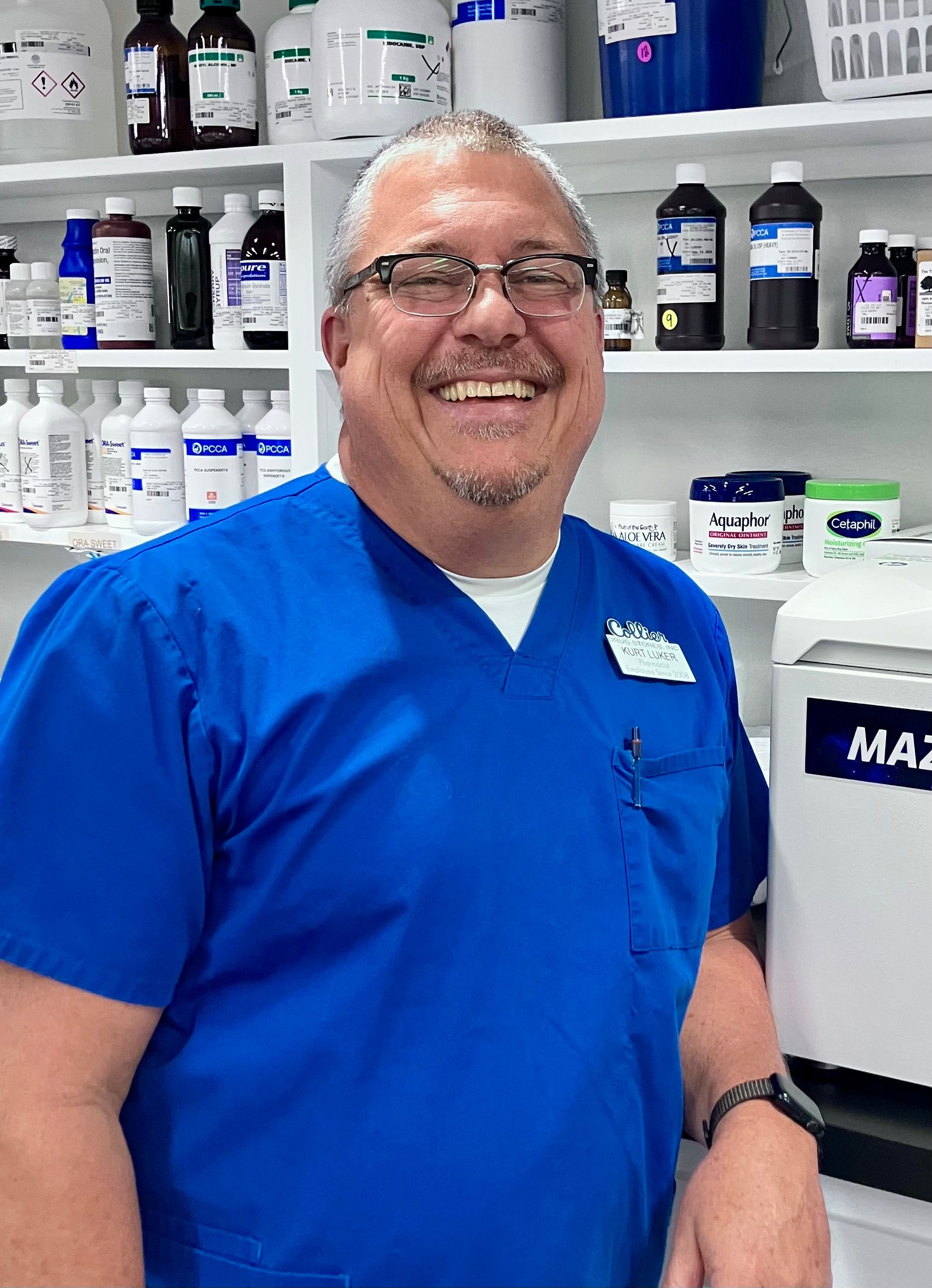A man with a beard is wearing a white lab coat and blue scrubs.